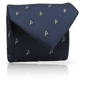 Op de afbeelding: Een marineblauwe stropdas met een herhaald patroon van witte en grijze gestileerde 'A'-vormen. De stropdas is opgevouwen en lijkt gemaakt van een gladde stof, met een lichte glans. Een klassiek en elegant accessoire.