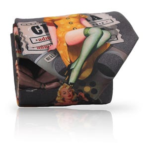 Può includere: Una cravatta piegata con un design vintage pin-up. La cravatta presenta una donna in abito giallo e calze verdi, con uno sfondo di bobina cinematografica e biglietto retrò. Il design è stampato su un tessuto grigio scuro.