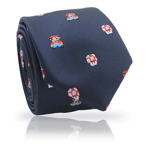 Puede incluir: Una corbata enrollada de color azul marino con un patrón repetido de personajes y hongos de videojuegos pixelados en rojo, blanco y azul. La corbata está hecha de una tela suave y tiene un ligero brillo.