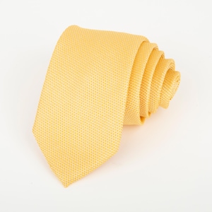 May include: A solid yellow necktie featuring a fine, textured weave pattern. The necktie is rolled into a spiral shape, displaying the pointed end and the layered folds of the fabric. The material has a consistent, bright yellow color throughout.