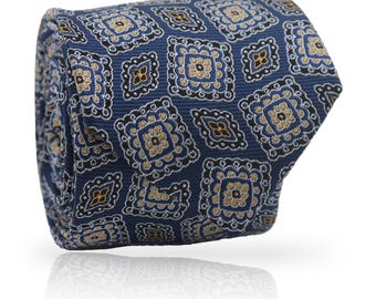 May include: Rolled navy blue tie with a repeating pattern of square floral designs in gold, black, and light blue. The tie is made of a textured fabric and is displayed on a white background.