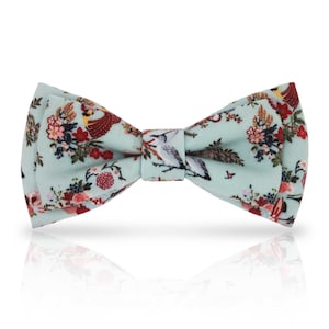 Könnte beinhalten: Hellblaue Fliege mit Blumen- und Vogelmuster. Die Fliege hat ein sich wiederholendes Muster aus Blumen, Vögeln und Blättern in Rot-, Rosa- und Brauntönen. Ein klassisches Accessoire für formelle oder halbformelle Kleidung, ca. 12 cm breit.