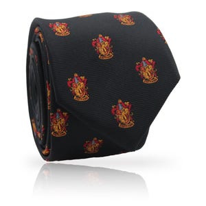 Peut inclure: Une cravate noire roulée avec un motif répété d'un blason rouge, or et blanc. Le blason comprend un écusson, un lion et les mots "GRYFFINDOR". La cravate est en tissu tissé.