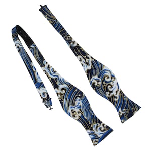 May include: A blue bow tie with a wave pattern in white and gold. The bow tie is made of fabric and has an adjustable strap. The wave pattern is a repeating design across the bow tie.