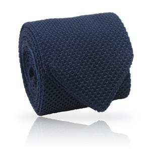 May include: A rolled navy blue knitted tie. The tie is made of a textured fabric and is displayed against a white background. The tie's end is visible, showing its shape.