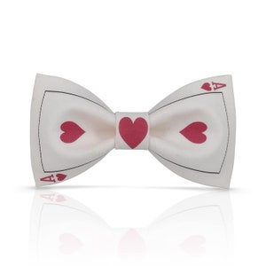 Puede incluir: Pajarita blanca con un diseño de as de corazones rojo. La pajarita tiene un contorno negro y el as de corazones está en el centro de la pajarita.