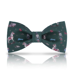 May include: A green bow tie featuring a festive pattern of toy soldiers, rocking horses, and other Christmas-themed toys.
