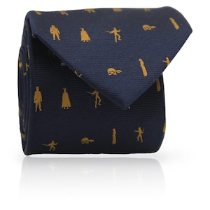Puede incluir: Corbata azul marino con un patrón repetido de figuras doradas. Las figuras incluyen personas, instrumentos musicales y otras formas. La corbata está doblada y tiene un ligero brillo.