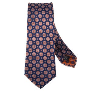 May include: A navy blue silk tie with a repeating pattern of orange and white floral designs. The tie is a classic width and features a pointed end. The fabric has a subtle sheen.