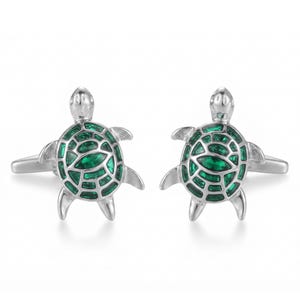 May include: A pair of silver-toned cufflinks shaped like sea turtles. Each turtle features a polished silver metal frame with a shell inlay composed of multiple small, vibrant green stones arranged in a mosaic pattern across the back.