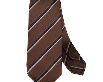 Può includere: Cravatta marrone a righe. La cravatta presenta un motivo a righe marroni, blu navy e bianco sporco. Il tessuto è liscio, adatto per occasioni formali. Un accessorio classico.