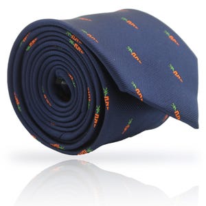May include: Rolled navy blue tie with a repeating pattern of orange carrots and green tops. The tie is made of a smooth fabric and is rolled up, showing the pattern and texture.