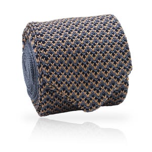 May include: Rolled-up knitted tie with a geometric pattern. The tie features a combination of navy blue, light blue, and tan colors. The knitted texture is visible, and the tie is displayed against a white background.