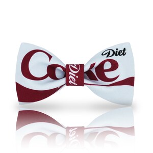 May include: White bow tie with a red and white Diet Coke logo. The bow tie has a white background with red lettering that says "Diet Coke" and a red band that says "Diet".