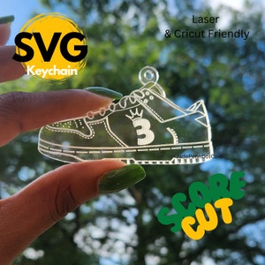 Puede incluir: Un llavero de acrílico transparente con forma de zapatilla deportiva con una corona y el número 3 en el lateral. El llavero está etiquetado como "SVG Keychain" y "Laser & Cricut Friendly".