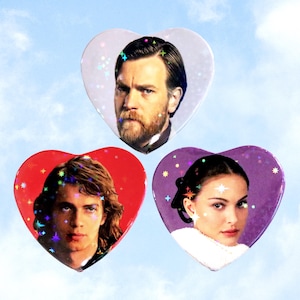 May include: Three heart-shaped buttons featuring portraits of characters from a science fiction film. The buttons have a holographic glitter effect and are set against a blue sky background. The text "ValentineMotel.com" is at the bottom.