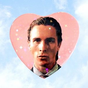 May include: A pink heart-shaped sticker featuring a portrait of a man against a blue sky background. The heart has holographic star accents and the text "ValentineMotel.com" at the bottom.