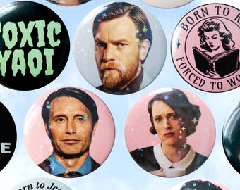 May include: A selection of round pin badges with diverse designs. Some badges feature portraits of actors, while others display text such as "TOXIC YAOI" and "BORN TO READ, FORCED TO WORK". The badges have a glossy finish and are decorated with iridescent glitter.