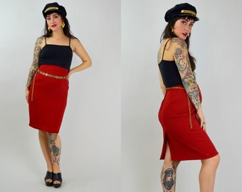 May include: A woman wearing a red skirt with a gold chain belt and a black tank top. She is also wearing a black sailor hat and has tattoos on her arms.