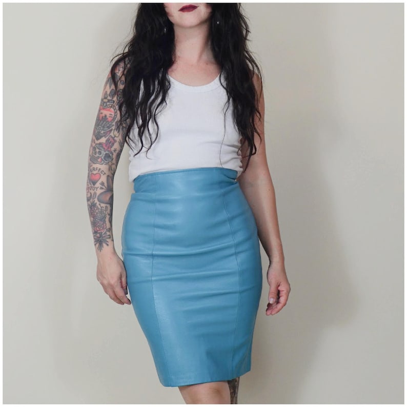 May include: A light blue leather pencil skirt. The skirt is a classic knee-length design with a high waist. The skirt is a solid colour. The model is wearing a white vest top. The skirt is approximately 60 cm in length.