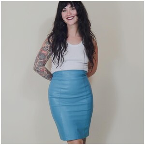 May include: A light blue pencil skirt. The skirt is made of a smooth material and has a high waist. The skirt is knee-length and has a fitted silhouette. The skirt is a solid colour and has a simple design.