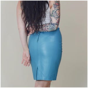 May include: A light blue leather pencil skirt. The skirt has a high waist and a back slit. The skirt is made of a smooth, shiny leather material. The skirt is knee-length.