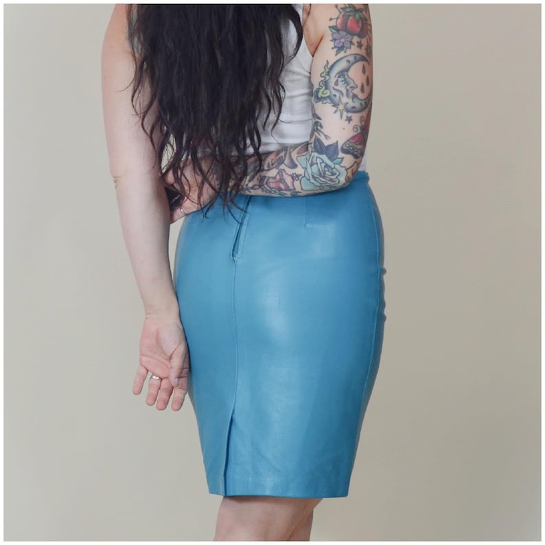 May include: A light blue leather pencil skirt. The skirt has a high waist and a back slit. The skirt is made of a smooth, shiny leather material. The skirt is knee-length.