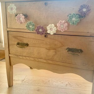 May include: A wooden dresser with two drawers and a crocheted flower garland in shades of pink, green, and white.