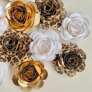 Op de afbeelding: Een assortiment van papieren bloemen in verschillende kleuren en patronen. De bloemen zijn gemaakt van papier en hebben een gelaagd, 3D-effect. De bloemen zijn in verschillende kleuren, waaronder wit, goud en bruin. De bloemen zijn in een cirkelvormige opstelling gerangschikt.