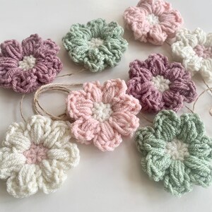 May include: A garland of crocheted flowers in shades of pink, green, and white. The flowers are strung together with twine and are perfect for adding a touch of handmade charm to any space.