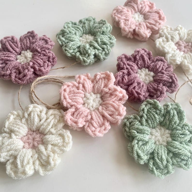 May include: A garland of crocheted flowers in shades of pink, green, and white. The flowers are strung together with twine and are perfect for adding a touch of handmade charm to any space.