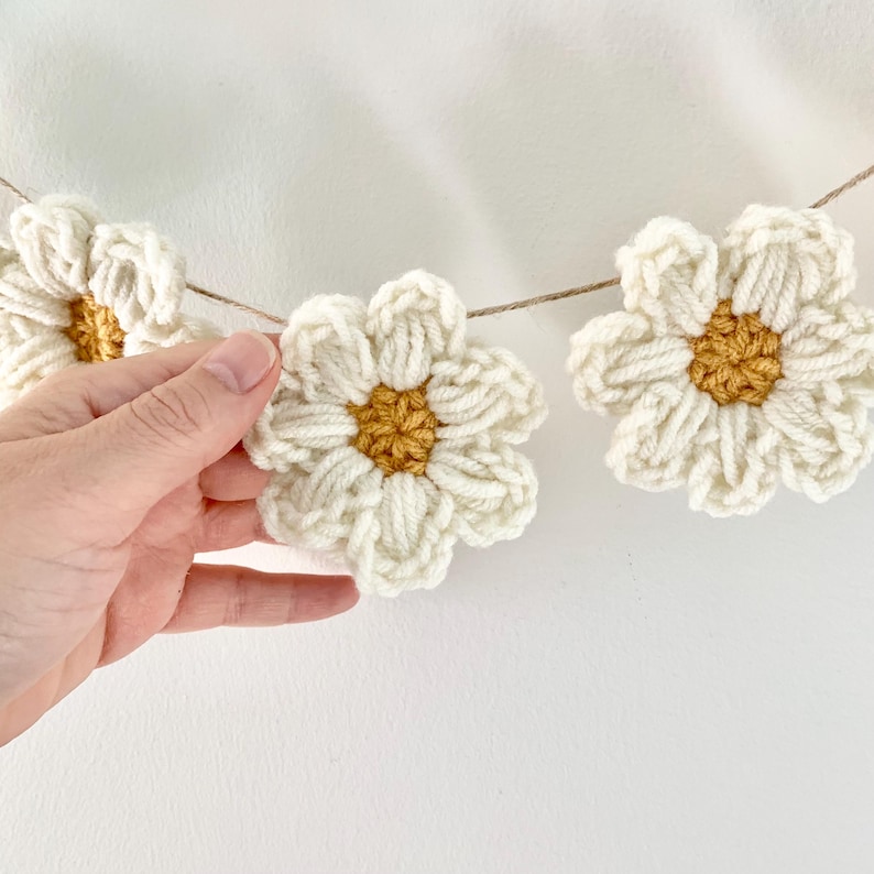 May include: A garland of crocheted white daisies with yellow centers. The daisies are strung together with twine.