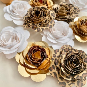 Op de afbeelding: Een assortiment van papieren bloemen in verschillende kleuren en patronen. De bloemen zijn gemaakt van papier en hebben een gelaagd, 3D-effect. De bloemen zijn in verschillende kleuren, waaronder wit, goud en bruin. De bloemen zijn in een cluster gerangschikt, en sommige bloemen hebben een luipaardprint.