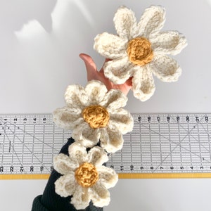 May include: Three crocheted white daisy flowers with yellow centers. The flowers are arranged in a row, with the largest flower at the top and the smallest flower at the bottom.