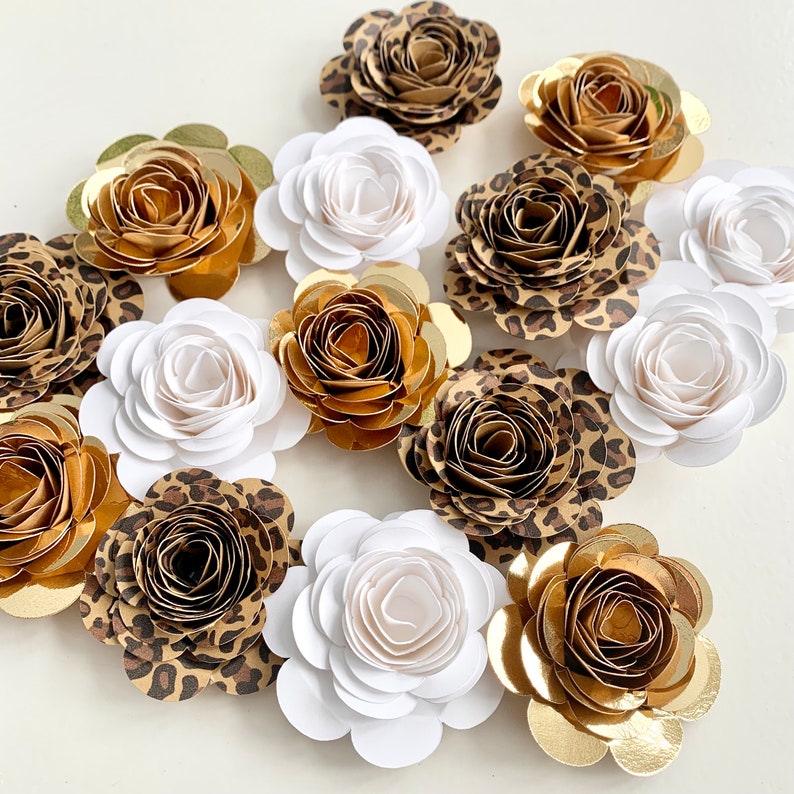 Op de afbeelding: Een verzameling van 12 papieren bloemen in verschillende kleuren en patronen, waaronder wit, goud, bruin en luipaardprint. De bloemen zijn allemaal gemaakt van papier en hebben een delicate, gelaagde uitstraling.
