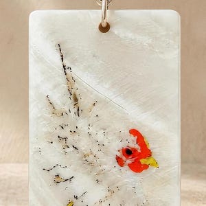 May include: A rectangular white pendant featuring an inlaid design of a bird with a bright orange head and yellow beak, accented by black speckles on its body. The pendant is suspended from a silver-toned metal bail with an intricate pattern.