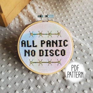 Peut inclure: Un modèle de point de croix pour un cerceau avec un fond ombré arc-en-ciel et un texte noir qui dit "All Panic No Disco".