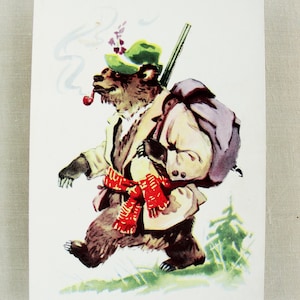 May include: A vintage postcard featuring a cartoon bear dressed in a coat, hat, and scarf, carrying a rifle and backpack. The bear is smoking a pipe and walking through a grassy area. The illustration has a whimsical, storybook style.