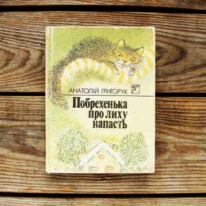 Peut inclure: Un livre de poche vintage avec une couverture jaune et une illustration en noir et blanc d'un chat. Le titre du livre est "Pobrezhenka pro lihu napasth" et l'auteur est "Anatoliy Grigoruk".