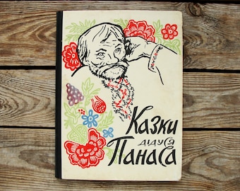May include: A vintage book cover with a black and white illustration of a man with a beard and mustache. The cover is decorated with red, green, and blue flowers. The title of the book is "Kazki Dlya Ditey" in black lettering.