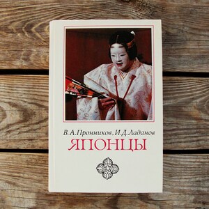 Op de afbeelding: Een wit boek met een rode titel die "ЯПОНЦЫ" (Japans) luidt. De omslag toont een zwart-witfoto van een vrouw in traditionele Japanse kleding die een waaier vasthoudt.