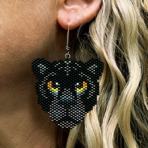 Boucles d'oreilles panthère noire, tissées avec des perles de rocaille Miyuki Delica, sur des crochets de boucle d'oreille français en argentium fait main dans une boîte en papier kraft.
