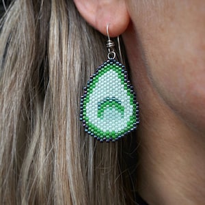 Boucles d'oreilles avocat, tissées avec des perles de rocaille Miyuki Delica, sur des crochets de boucles d'oreilles en argentium 93,5 dans une boîte en papier kraft.
