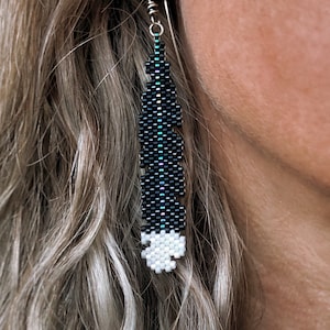 Mini boucles d'oreilles en plumes Huia, tissées avec des perles de rocaille Miyuki Delica, sur des crochets de boucles d'oreilles en argentium 93,5 français dans une boîte en papier kraft.