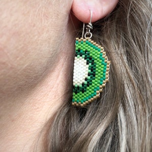 Boucles d'oreilles quart de kiwi, tissées avec des perles de rocaille Miyuki Delica, sur des crochets de boucle d'oreille français en argentium 93,5 dans une boîte en papier kraft.