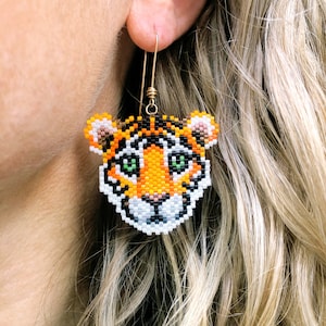 Boucles d'oreilles bébé tigre, tissées avec des perles de rocaille Miyuki Delica, sur des crochets de boucles d'oreilles français remplis d'or 14 carats dans une boîte en papier kraft.