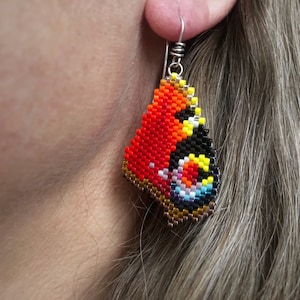 Boucles d'oreilles papillon paon, tissées avec des perles de rocaille Miyuki Delica, sur des crochets de boucles d'oreilles en argentium 93,5 dans une boîte en papier kraft.