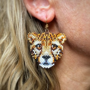 Orecchini a forma di cucciolo di ghepardo, intrecciati con perline Miyuki Delica, con ganci per orecchini francesi fatti a mano e riempiti in oro 14k, in una scatola di carta Kraft.