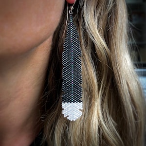 Boucles d'oreilles en plumes Huia, tissées avec des perles de rocaille Miyuki Delica, sur des crochets de boucles d'oreilles en argentium 93,5 français dans une boîte en papier kraft.
