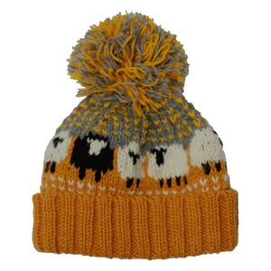 K&ouml;nnte beinhalten: Gestrickte Winterm&uuml;tze mit Schafmuster. Die M&uuml;tze hat einen senfgelben Rippenbund, eine grau-gelb gemusterte Krone und einen gro&szlig;en gelben Bommel. Die Schafe sind wei&szlig; und schwarz.